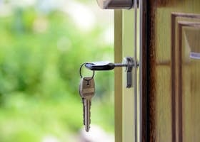 Key inserted in door lock against a blurred green background, symbolizing security and real estate.